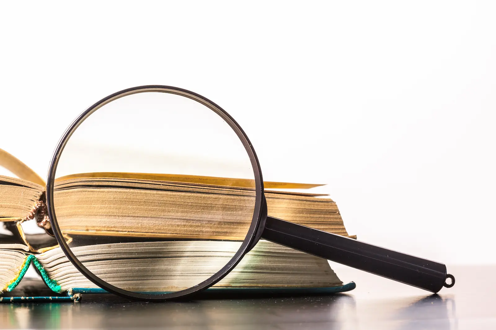 Loupe posée sur une pile de livres anciens, illustrant l'examen des différentes définitions du décrochage scolaire